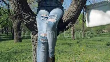 公园里有电话的女孩。 一个十几岁的女孩坐在一棵树上，拿着一部电话。 一个穿破牛仔裤的女孩坐在树上。